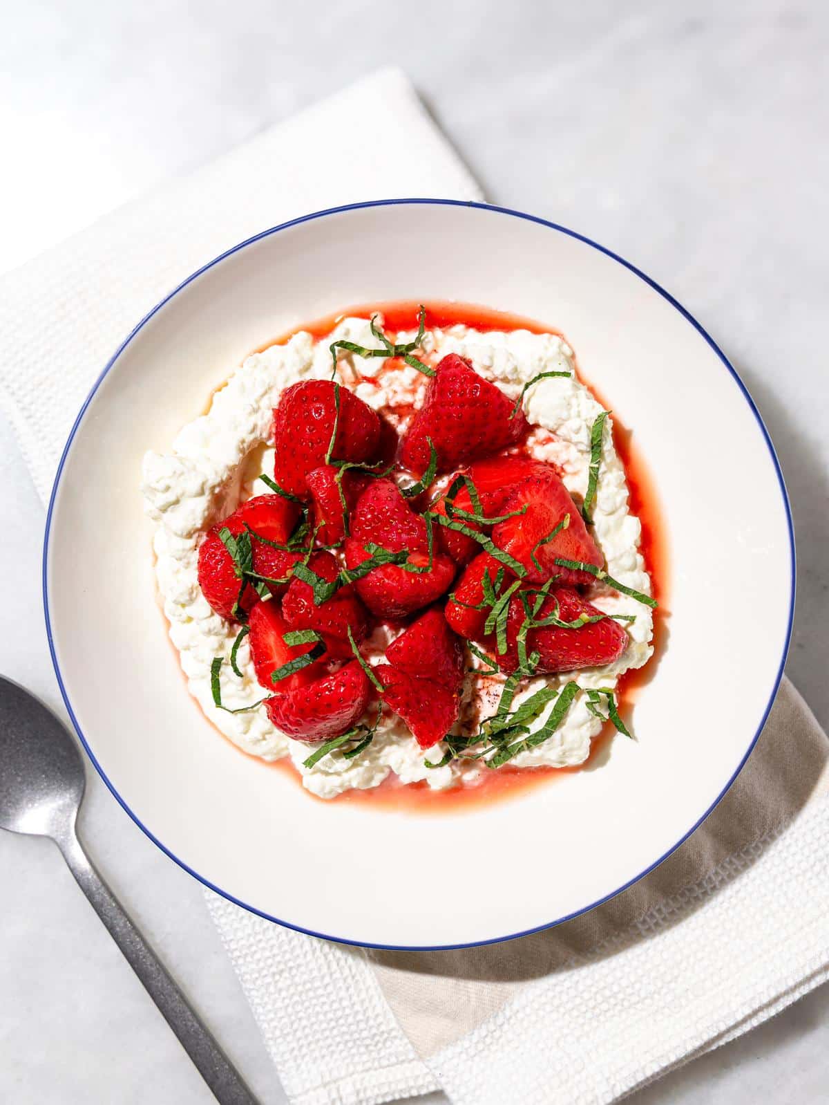 Cottage cheese bowl with strawberries topped with macerated strawberries, syrup, and fresh mint, with a spoon