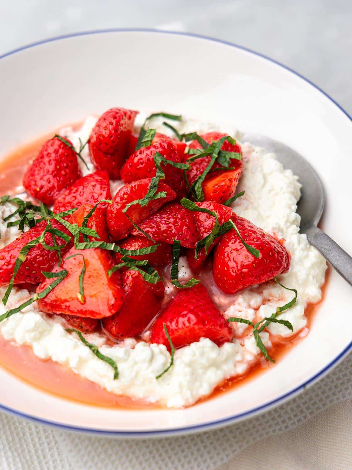 Close-up of a cottage cheese breakfast bowl with macerated strawberries, juice, and mint