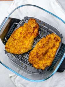 Two golden crispy sesame chicken cutlets in an air fryer