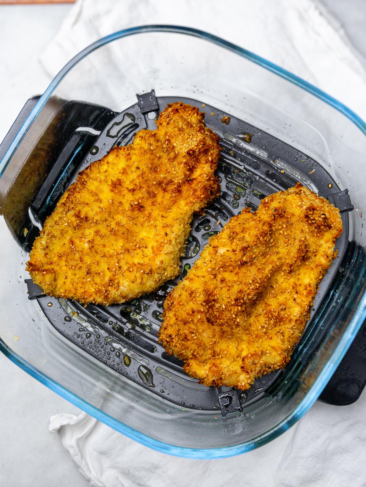 Two golden crispy sesame chicken cutlets in an air fryer