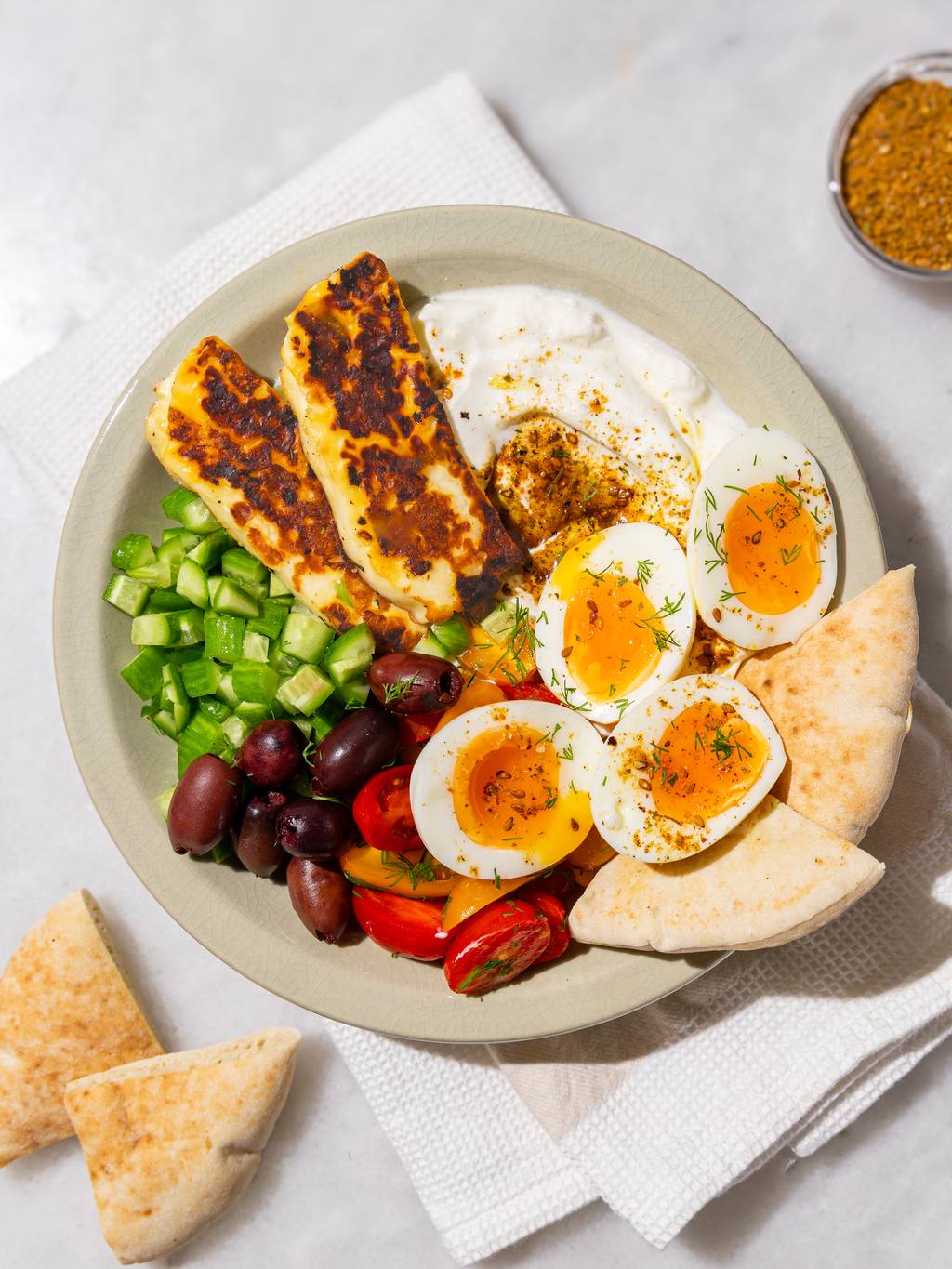Easy mediterranean breakfast plate with halloumi, jammy eggs, greek yogurt, and warm pita on the side