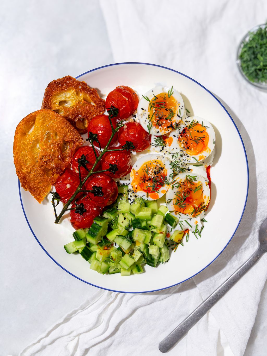 Greek yogurt breakfast bowl with eggs, cherry tomatoes, cucumber, and everything bagel seasoning