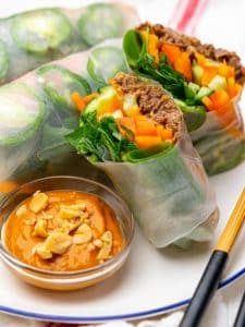Beef summer rolls cut to show the filling next to a bowl of spicy peanut sauce with crushed peanuts