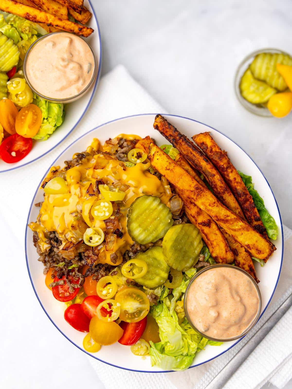 two high protein burger bowls meal prepped with beef, fries, tomatoes, pickles, and special sauce