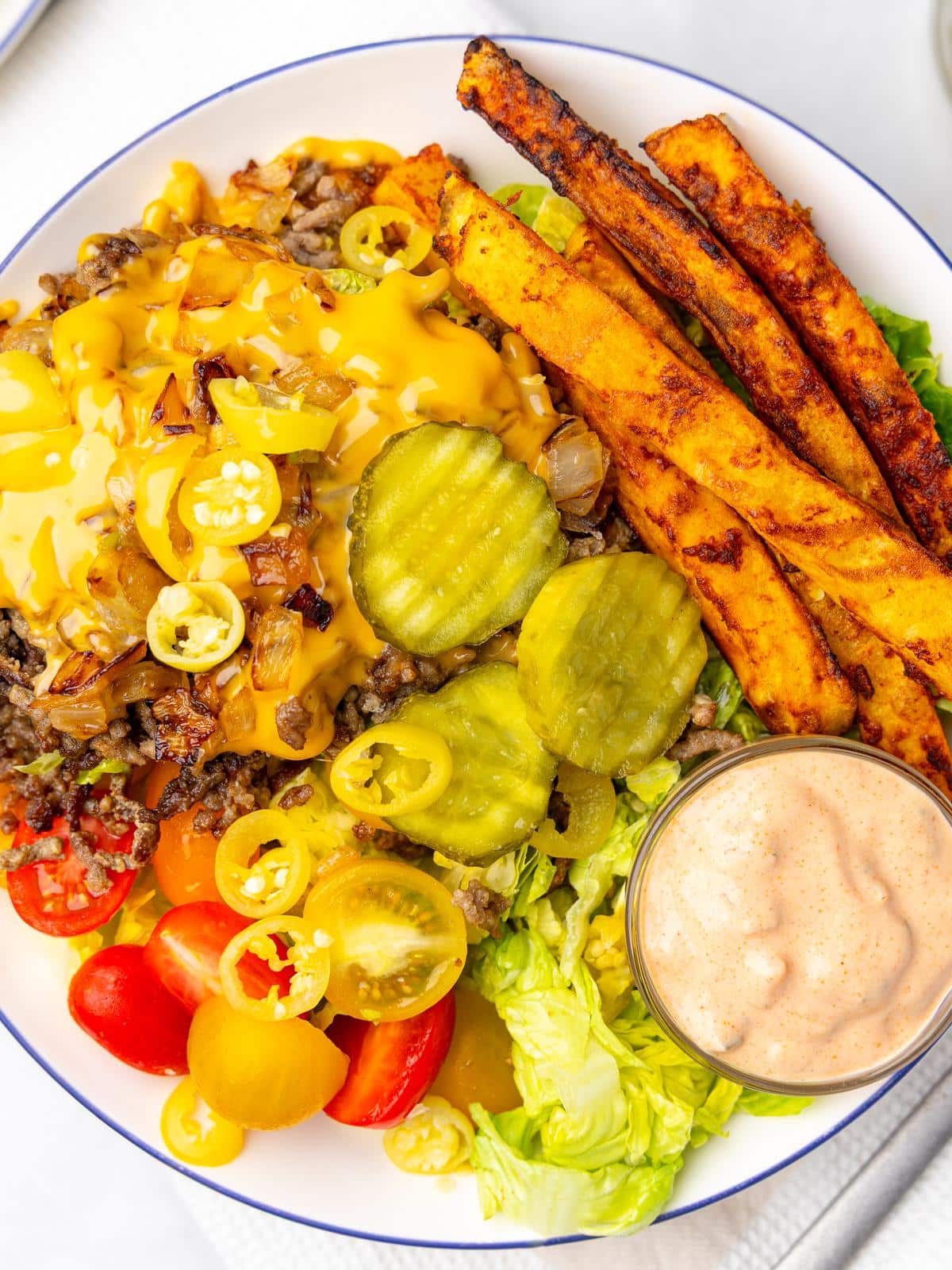 overhead close-up of a high protein cheeseburger bowl with melted cheese, beef, pickles, and air fryer fries