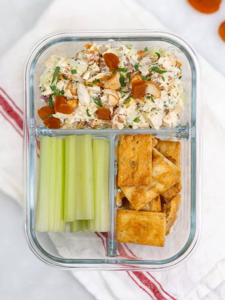 Apricot chicken salad meal prep container with celery sticks and pita crackers