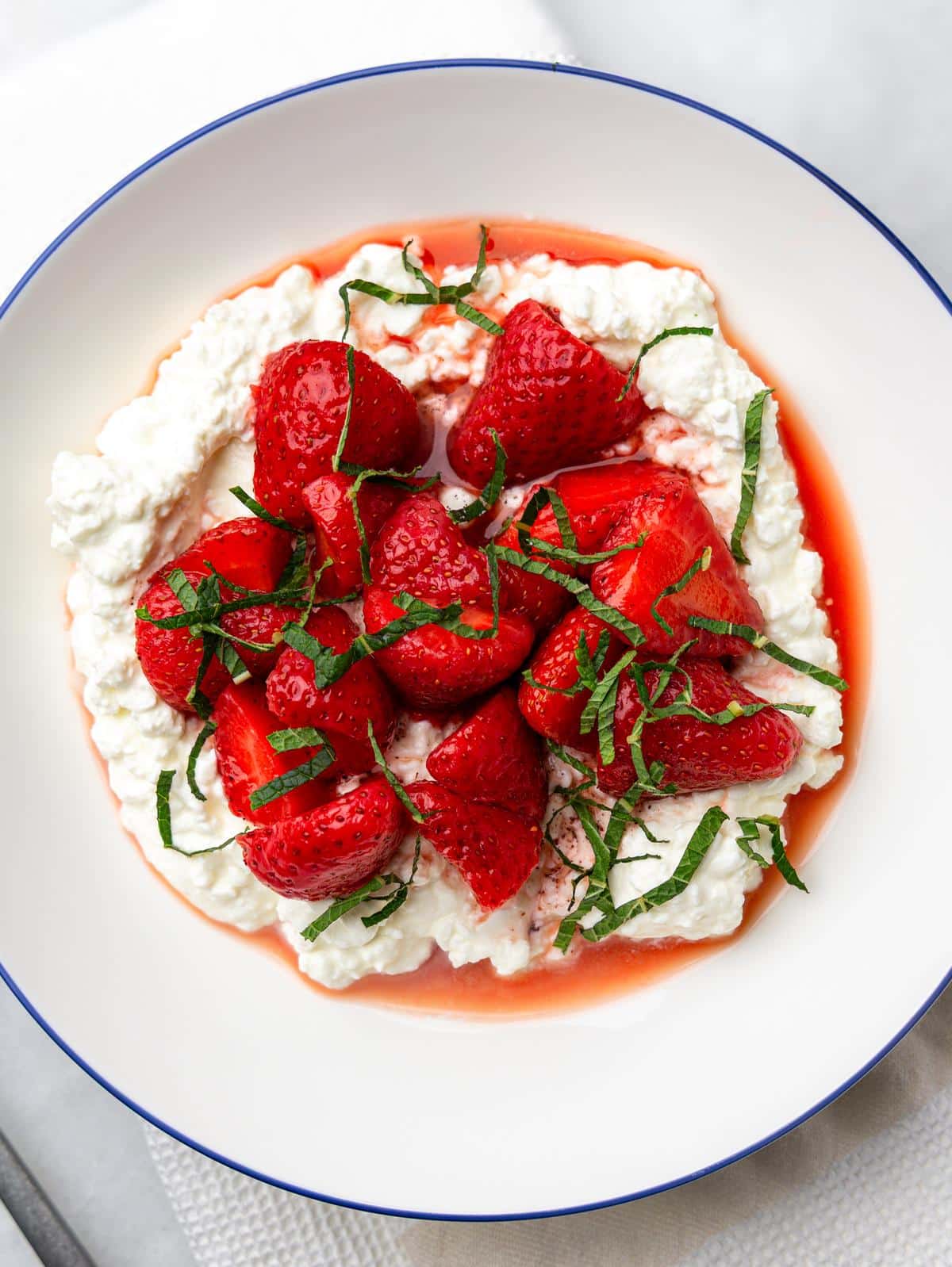Overhead high-protein cottage cheese bowl piled with juicy strawberries and fresh mint