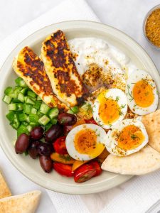 High-protein mediterranean breakfast plate with jammy eggs, halloumi, marinated tomatoes, olives, and za'atar yogurt