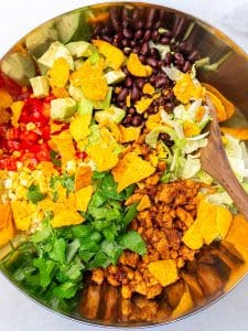 High-protein taco salad in a metal bowl with chipotle chicken, black beans, avocado, corn and crushed tortilla chips