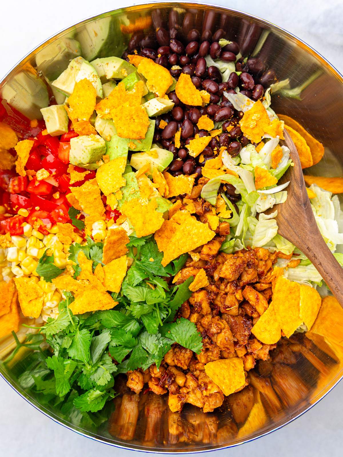 High-protein taco salad in a metal bowl with chipotle chicken, black beans, avocado, corn and crushed tortilla chips