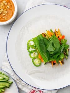Rice paper wrapper topped with beef, herbs, carrot, jalapeño, and bell pepper before rolling