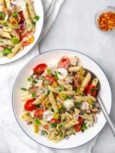 Two blue-rimmed bowls of italian grinder pasta salad with a spoon and red pepper flakes