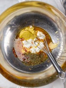 Creamy grinder dressing ingredients with greek yogurt, dijon, oregano, and red pepper flakes in a metal bowl