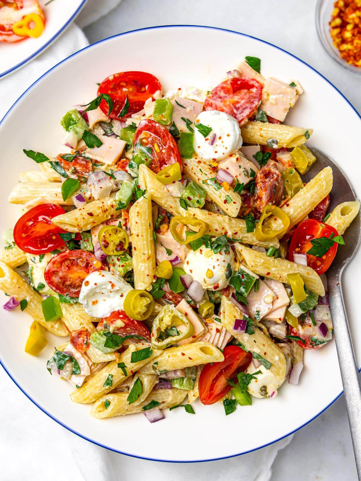 Two bowls of italian grinder pasta salad with creamy dressing, cherry tomatoes, and fresh herbs