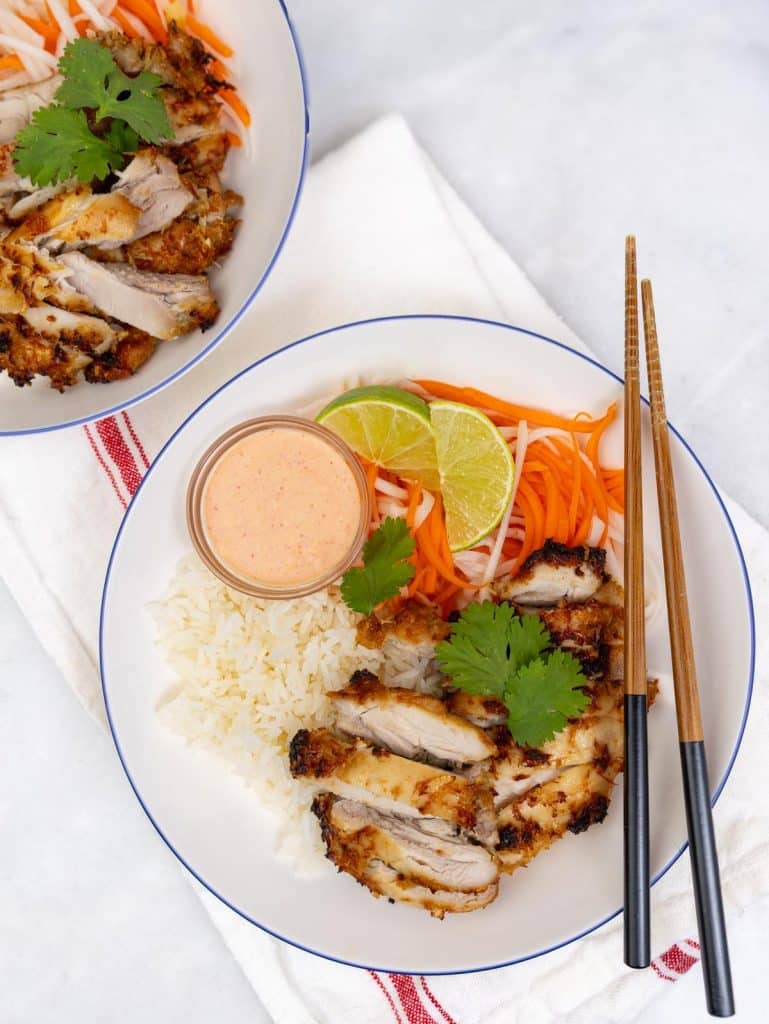 Two plates of lemongrass chicken rice bowls with sriracha mayo, pickled vegetables, and fresh lime