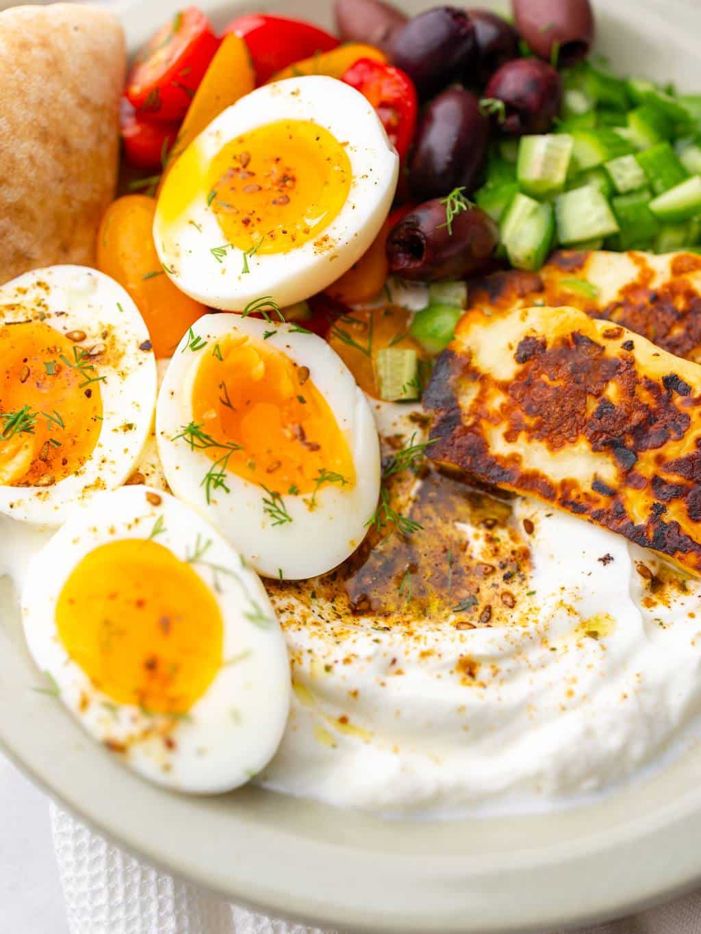 Jammy soft-boiled eggs cut open over za'atar greek yogurt with halloumi, olives, and cucumber