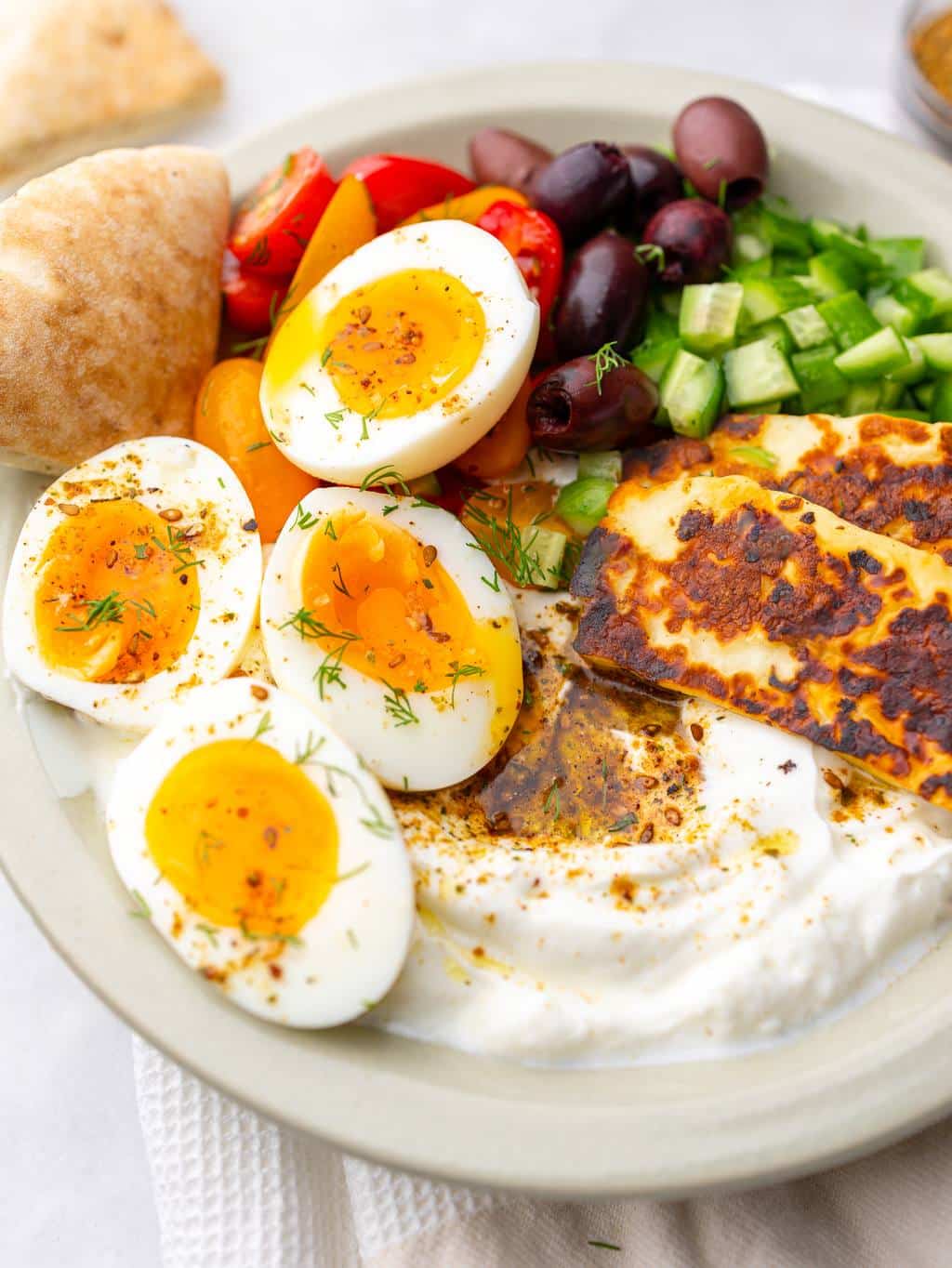Close-up of a mediterranean breakfast plate with jammy soft-boiled eggs, halloumi, and za'atar greek yogurt