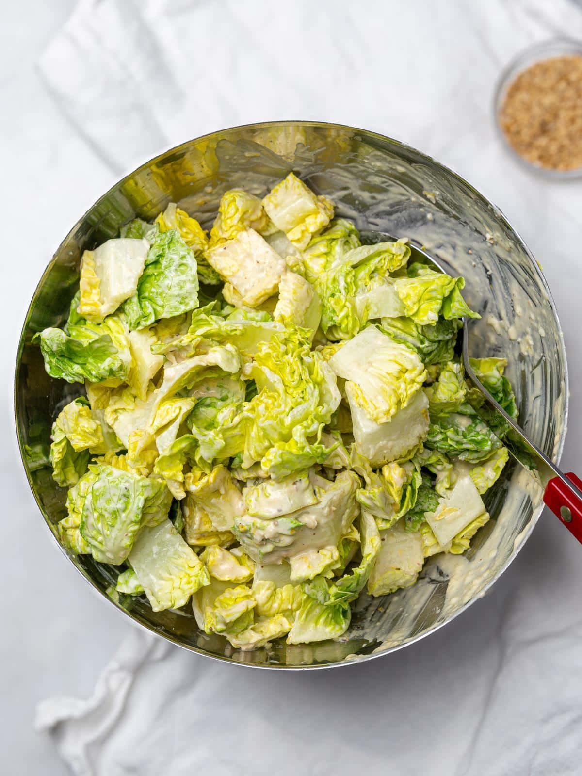 Chopped romaine tossed with creamy miso caesar dressing in a mixing bowl
