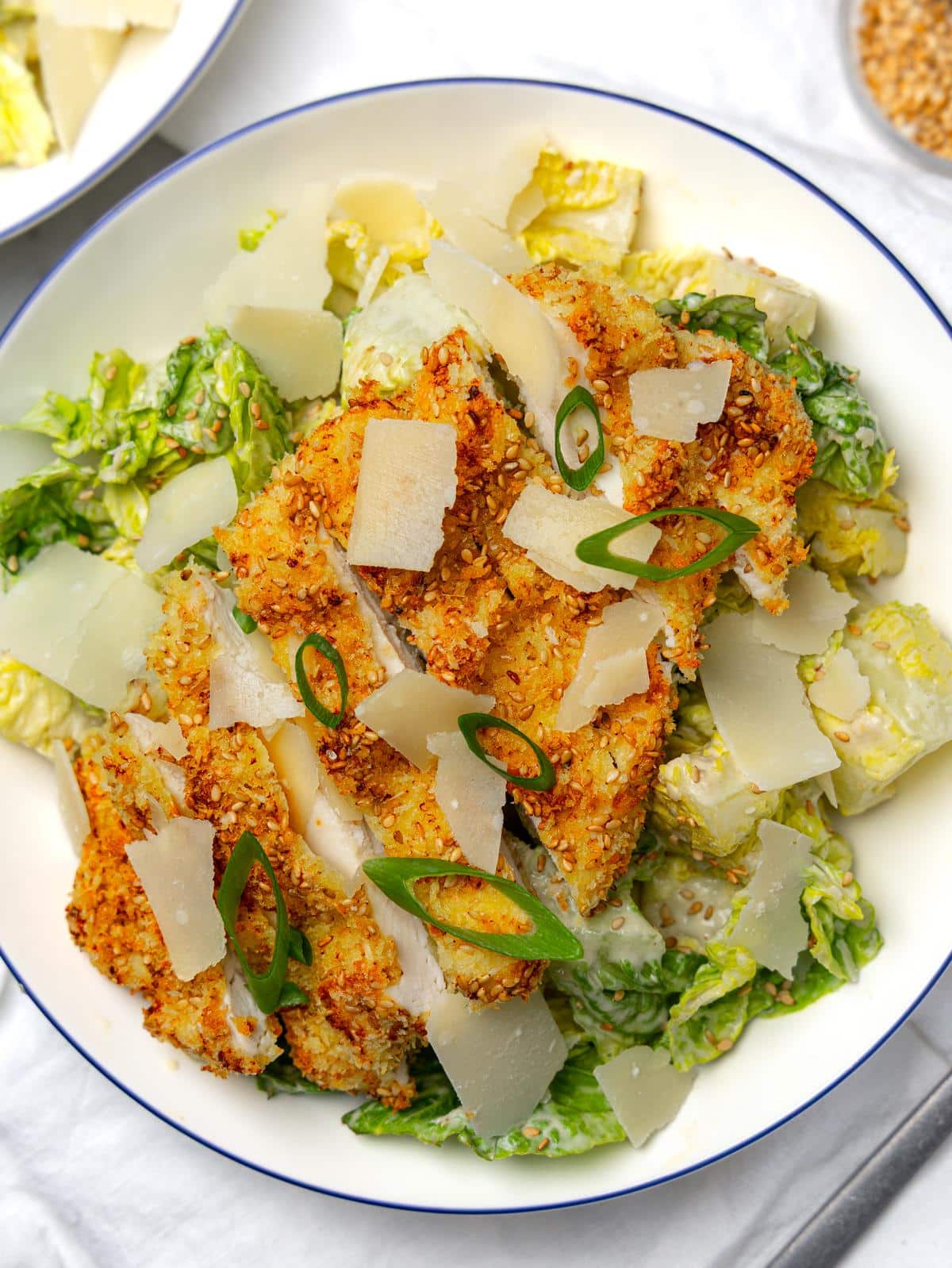 Overhead miso caesar salad with sliced crispy sesame chicken on romaine