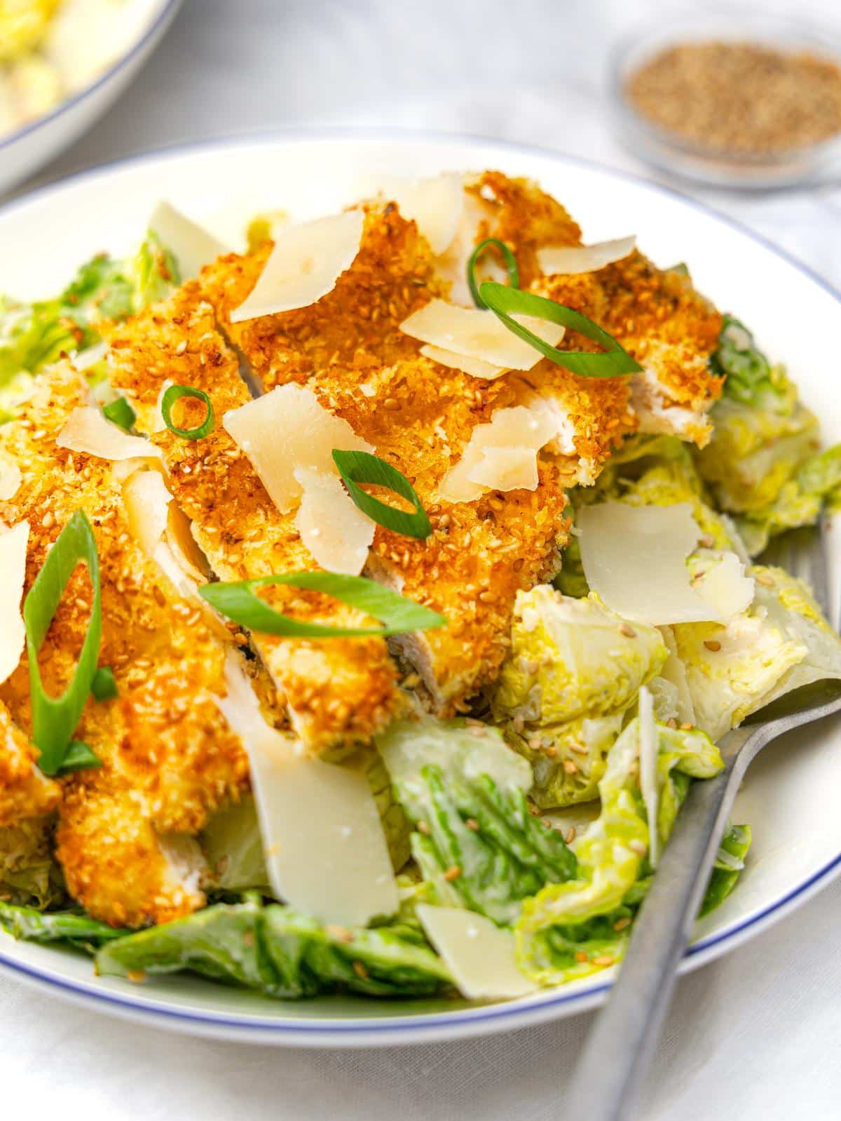 Miso caesar salad topped with crispy sesame chicken, shaved parmesan and green onion