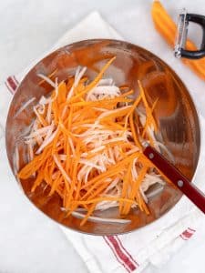 Julienned carrot and daikon ribbons in a metal mixing bowl ready to be quick pickled