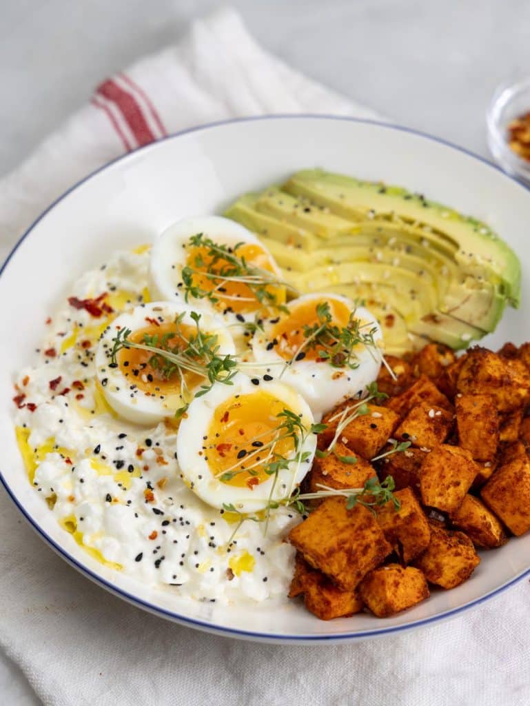 Close-up of a savory cottage cheese bowl with soft eggs, avocado slices, and sweet potato