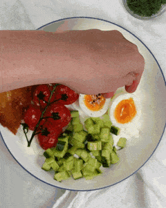 Sprinkling fresh dill over a savory greek yogurt breakfast bowl with jammy egg and tomatoes