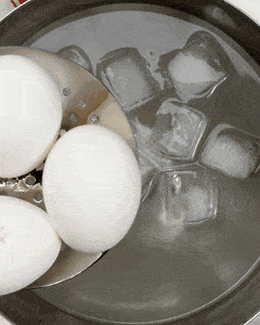 Soft-boiled eggs cooling in an ice bath with a slotted spoon