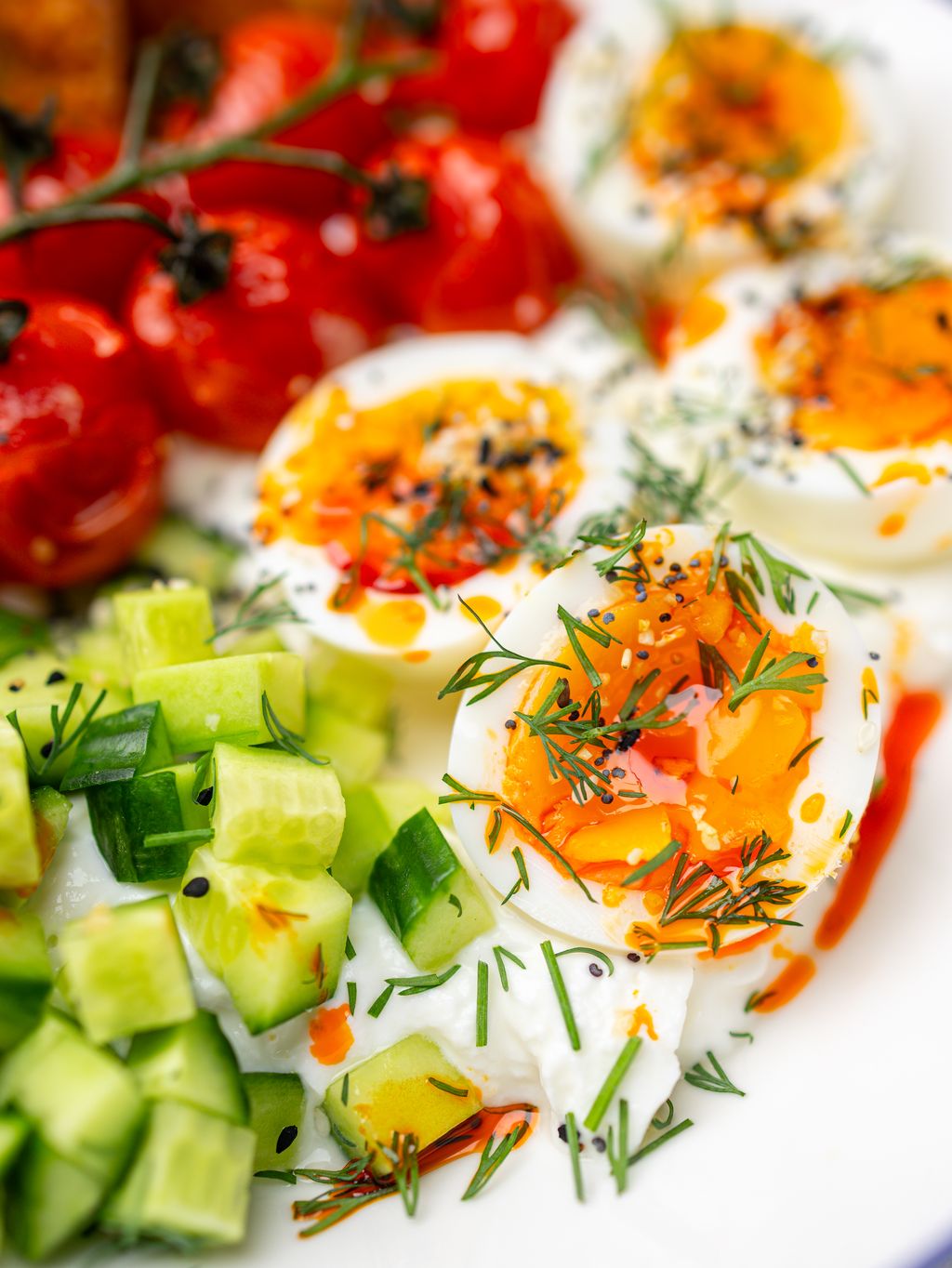 Overhead savory greek yogurt bowl with jammy eggs, vine tomatoes, diced cucumber, and toast