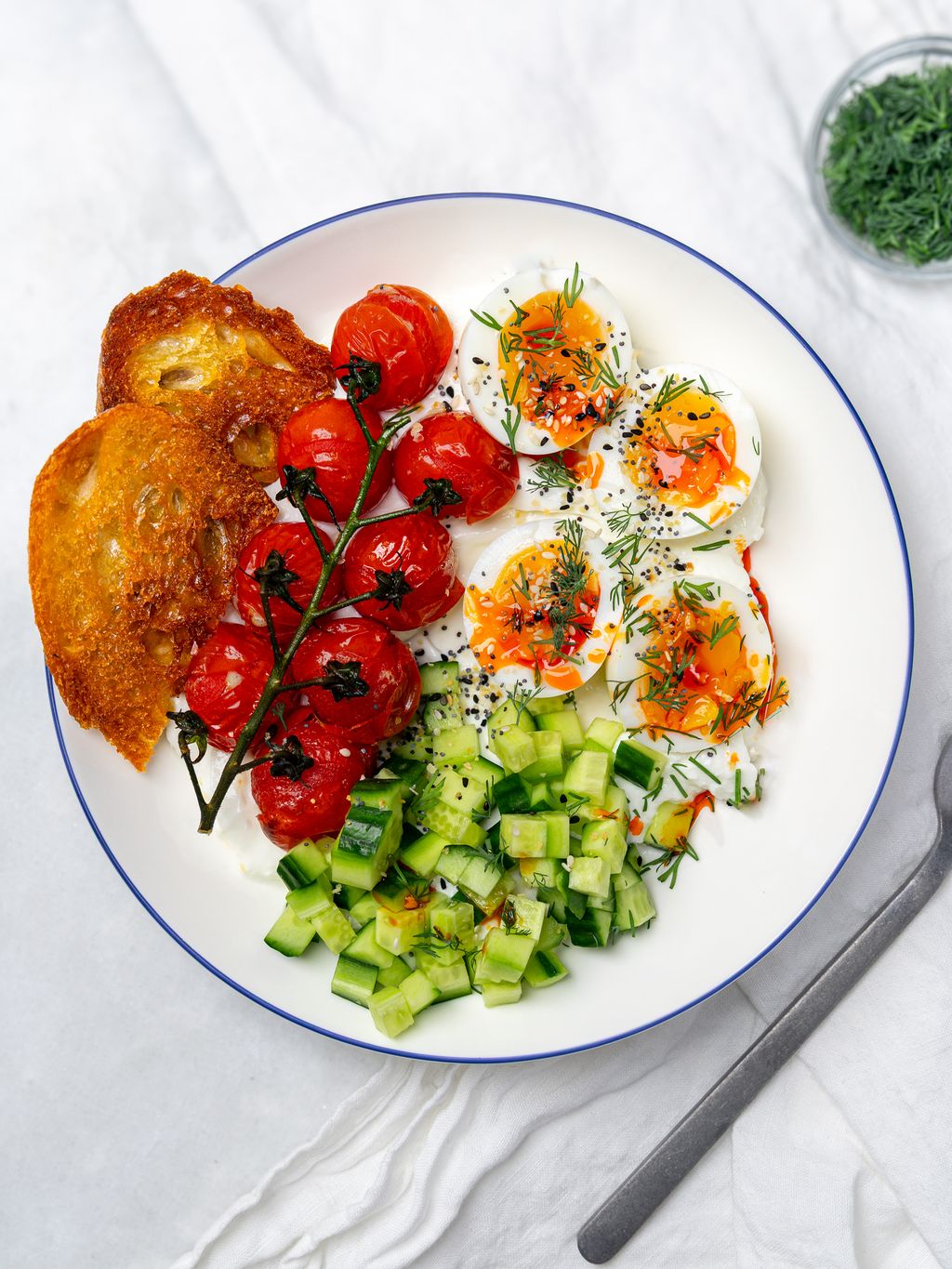 Savory greek yogurt bowl with jammy eggs, blistered cherry tomatoes, cucumber, and sourdough