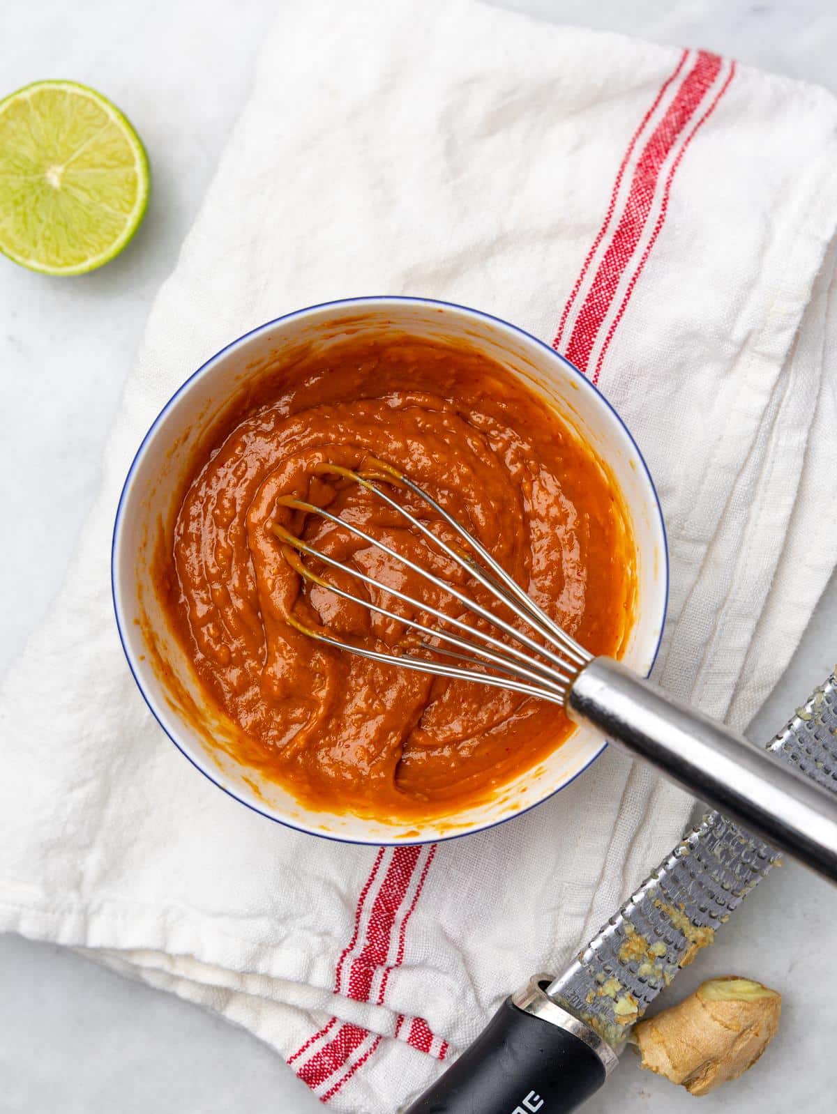 Spicy peanut sauce whisked in a bowl with lime and fresh ginger on the side