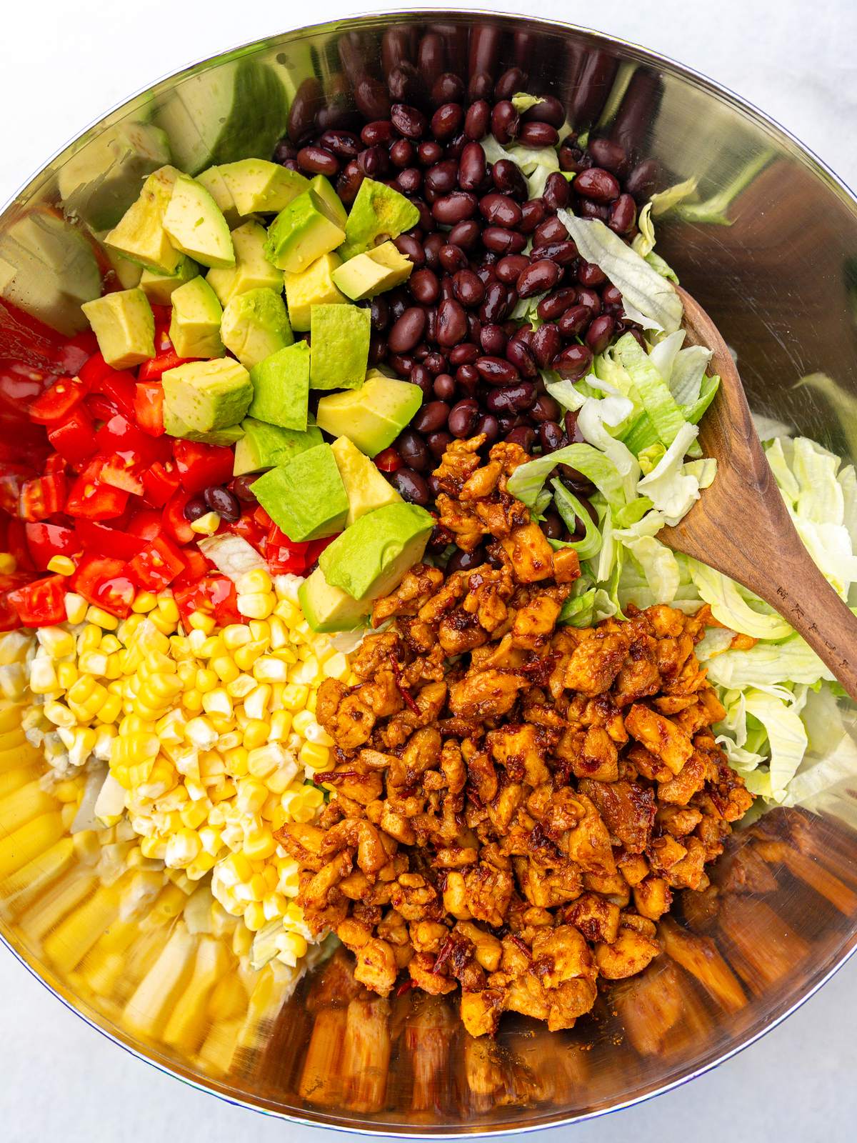 Taco salad ingredients in a metal bowl with chipotle chicken, black beans, avocado, corn and tomatoes