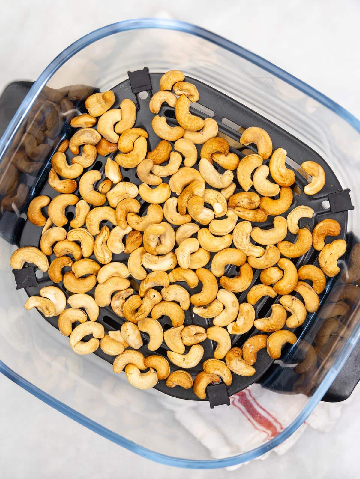 Toasted cashews in an air fryer basket for cashew chicken salad