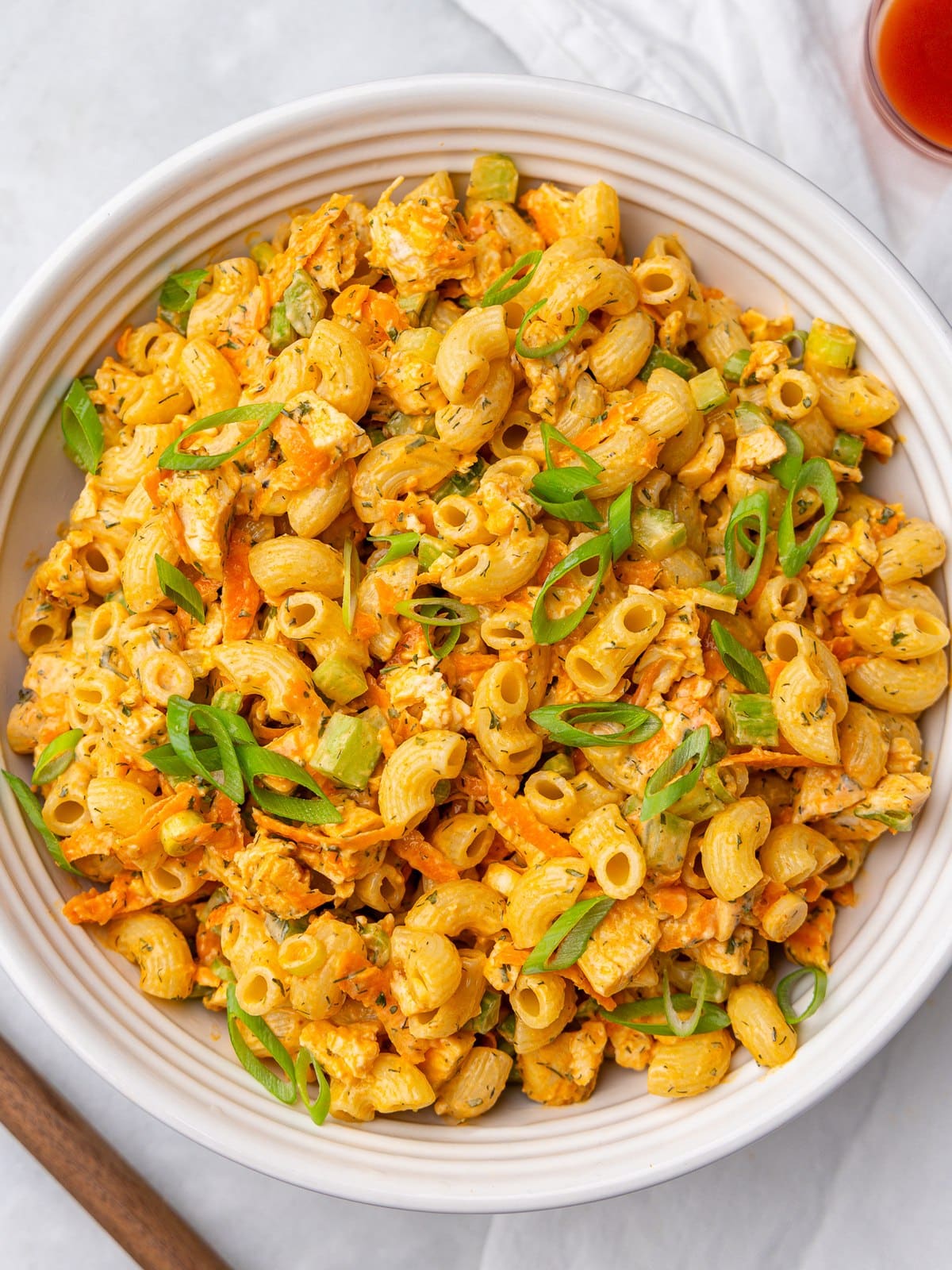 Healthy buffalo chicken pasta salad topped with green onions in a large white bowl