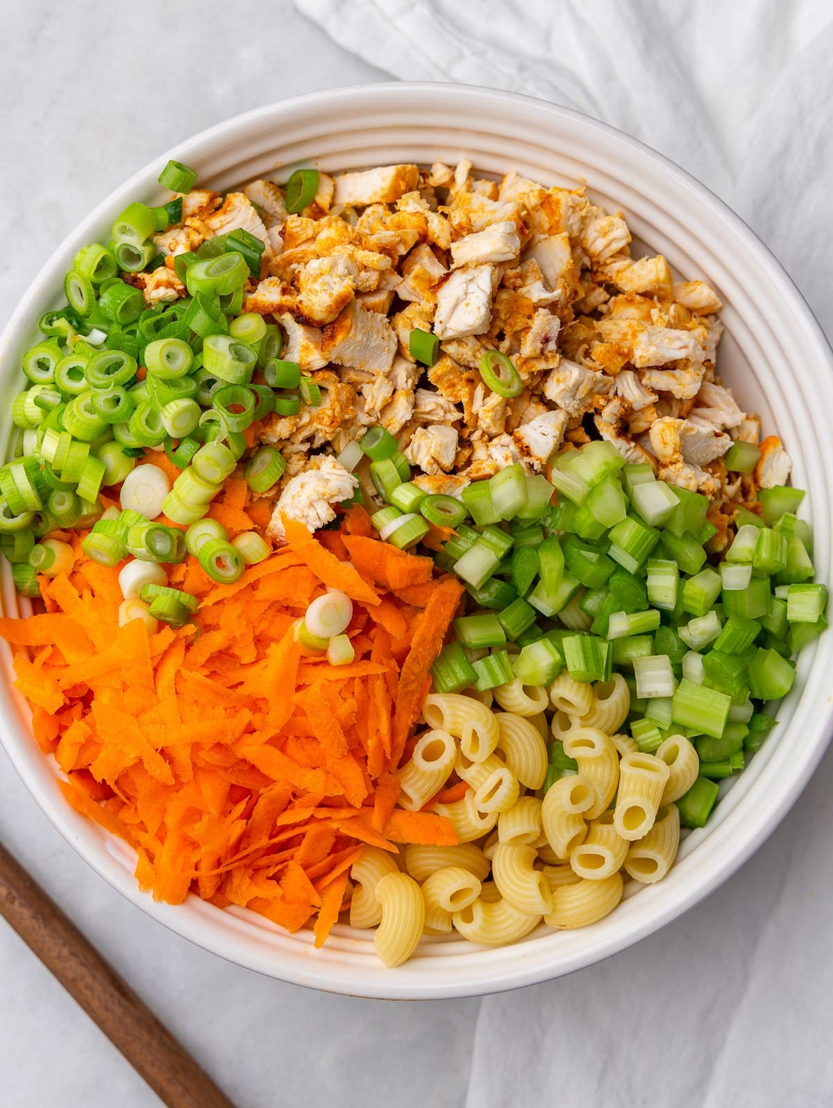 Chopped chicken, celery, shredded carrots, green onions and pasta in a white bowl