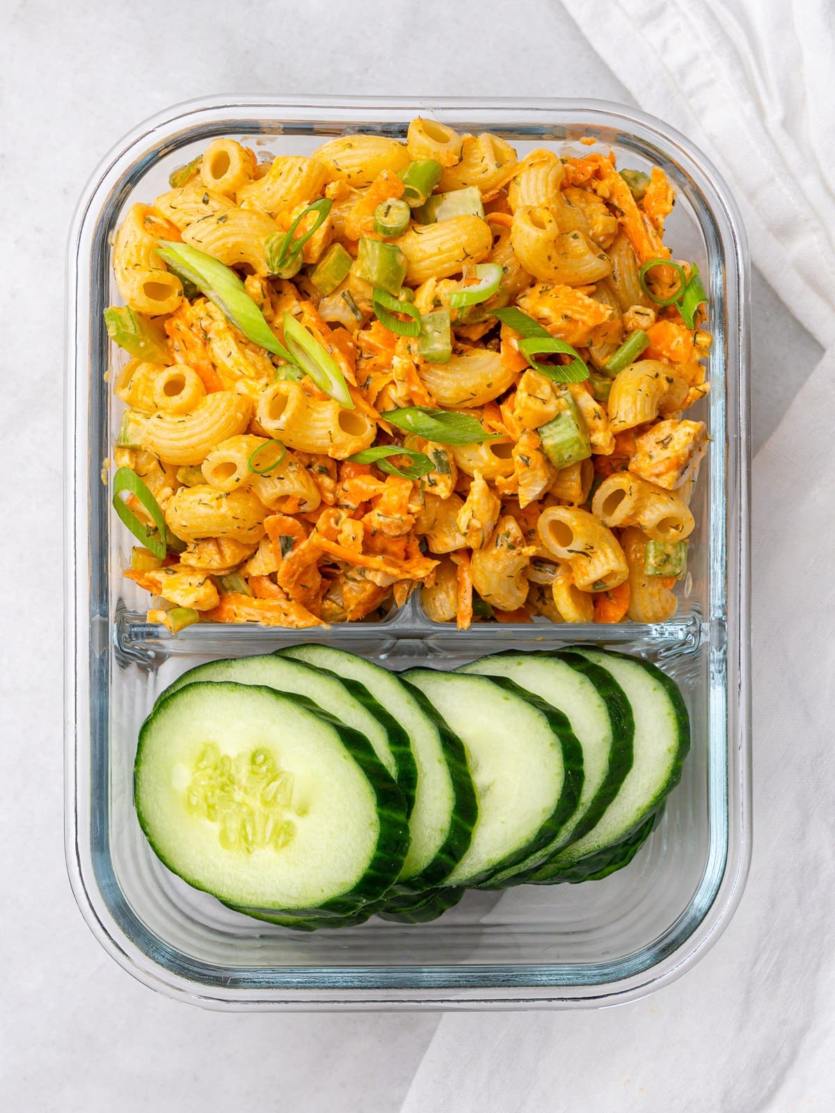 High-protein buffalo chicken pasta salad in a glass meal prep container with sliced cucumber