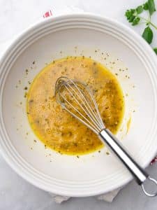 Whisked olive oil and red wine vinegar chickpea salad dressing in a white bowl