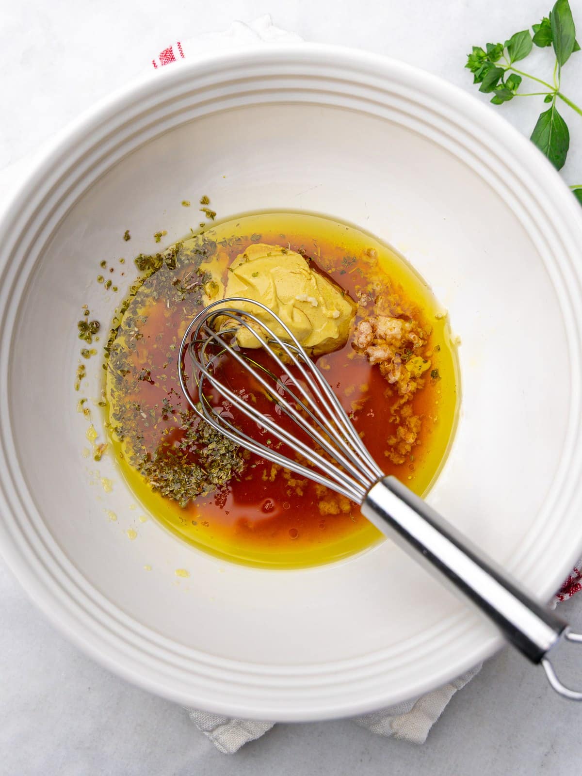 Chickpea salad dressing ingredients with olive oil, red wine vinegar, dijon mustard, garlic, and oregano in a white bowl