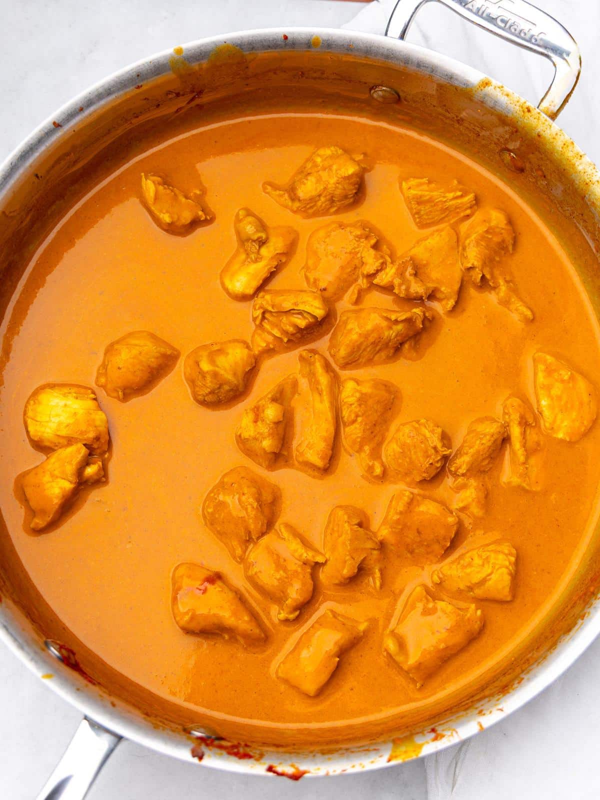Chicken simmering in a creamy coconut milk sauce in a skillet