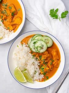 Two coconut chicken rice bowls with cucumber and lime on a white linen napkin