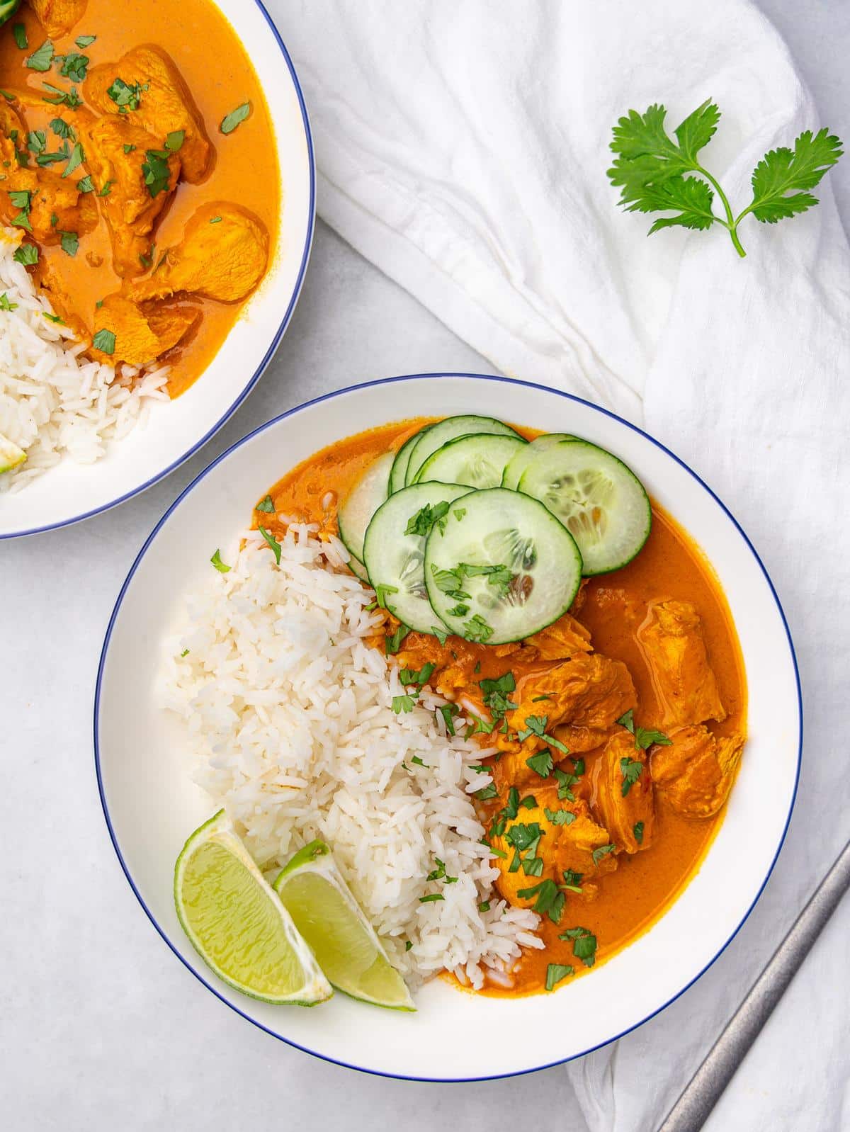 Two coconut chicken rice bowls with cucumber and lime on a white linen napkin