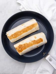 Two healthy breakfast burritos toasting seam side down in a dry skillet