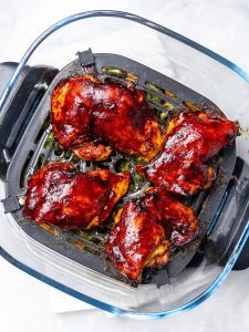 Teriyaki glazed chicken thighs cooking on top of broccoli in an air fryer basket
