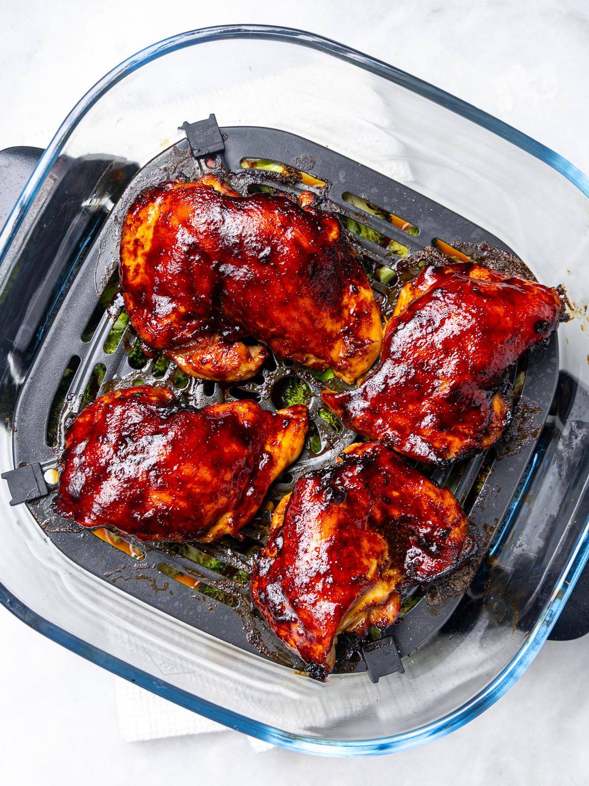 Teriyaki glazed chicken thighs cooking on top of broccoli in an air fryer basket