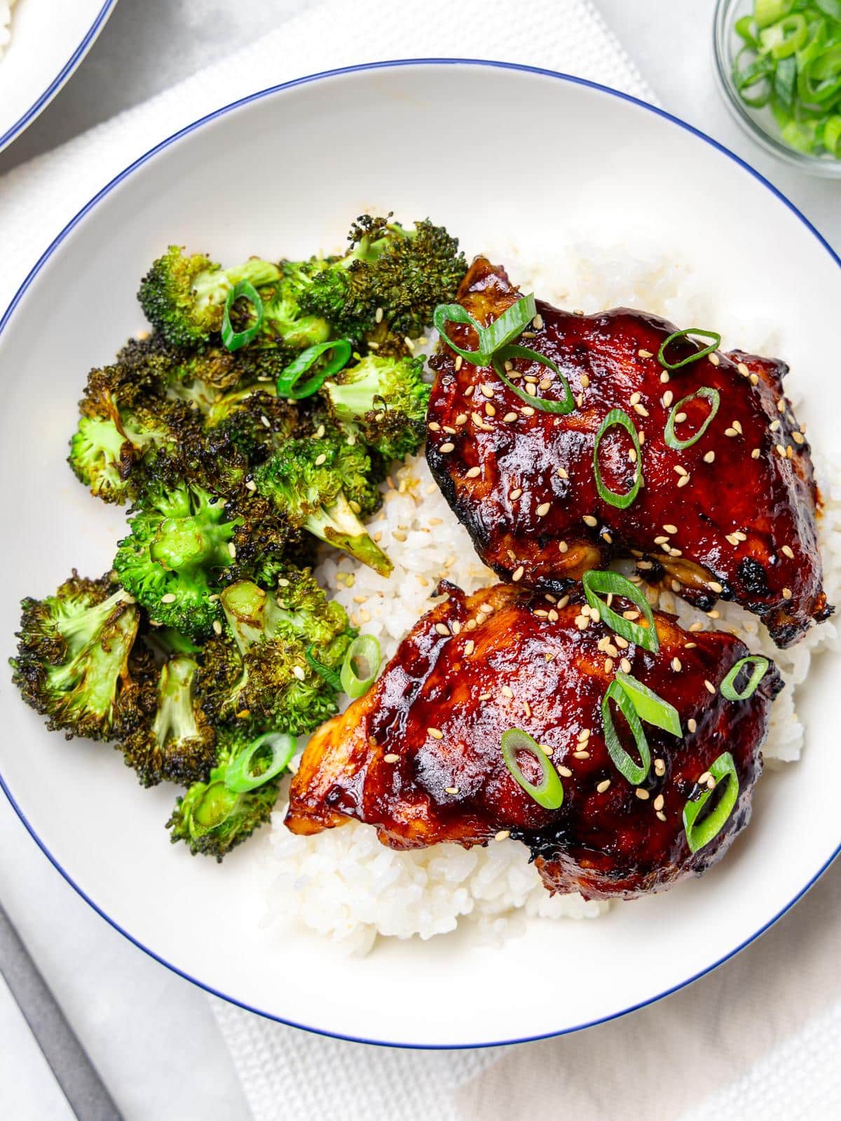 Close up of teriyaki glazed chicken thighs with sesame seeds and green onions over white rice