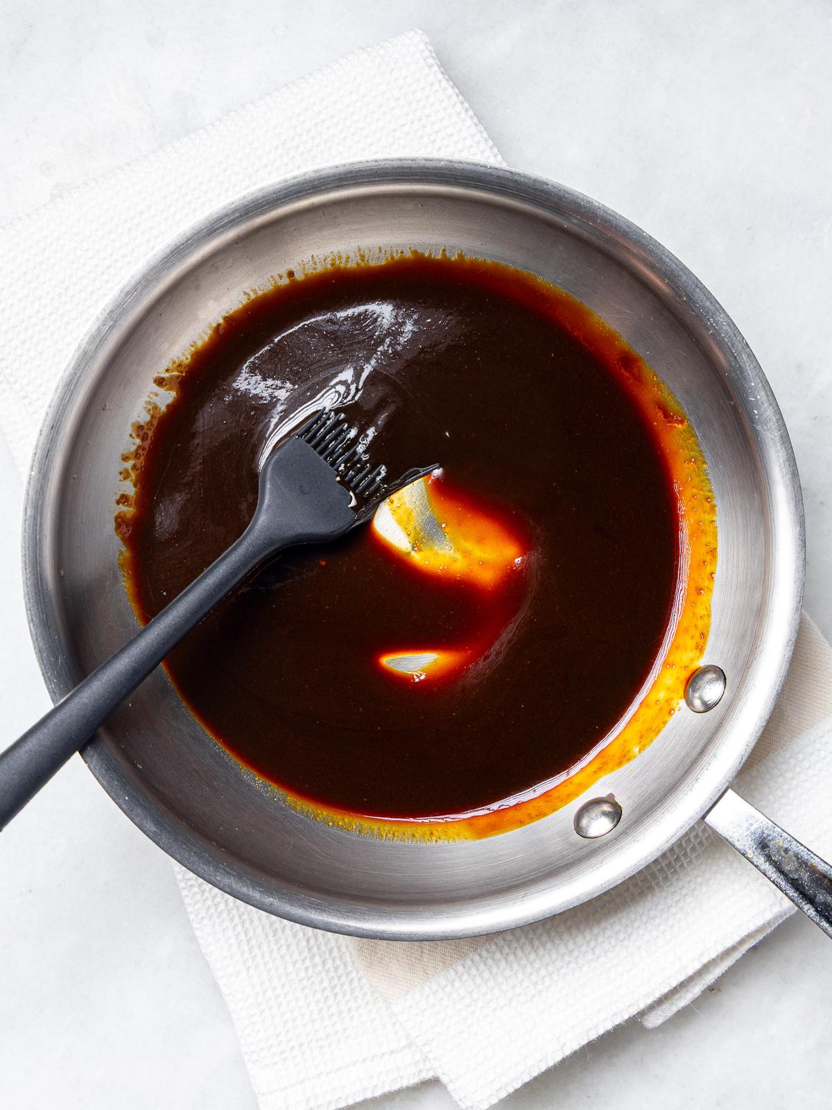 Thickened orange teriyaki sauce in a small saucepan with a basting brush