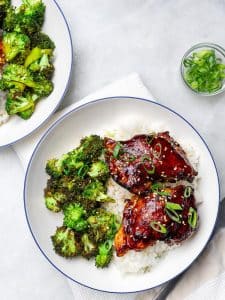 Two teriyaki chicken rice bowls with crispy broccoli and a small bowl of sliced green onions