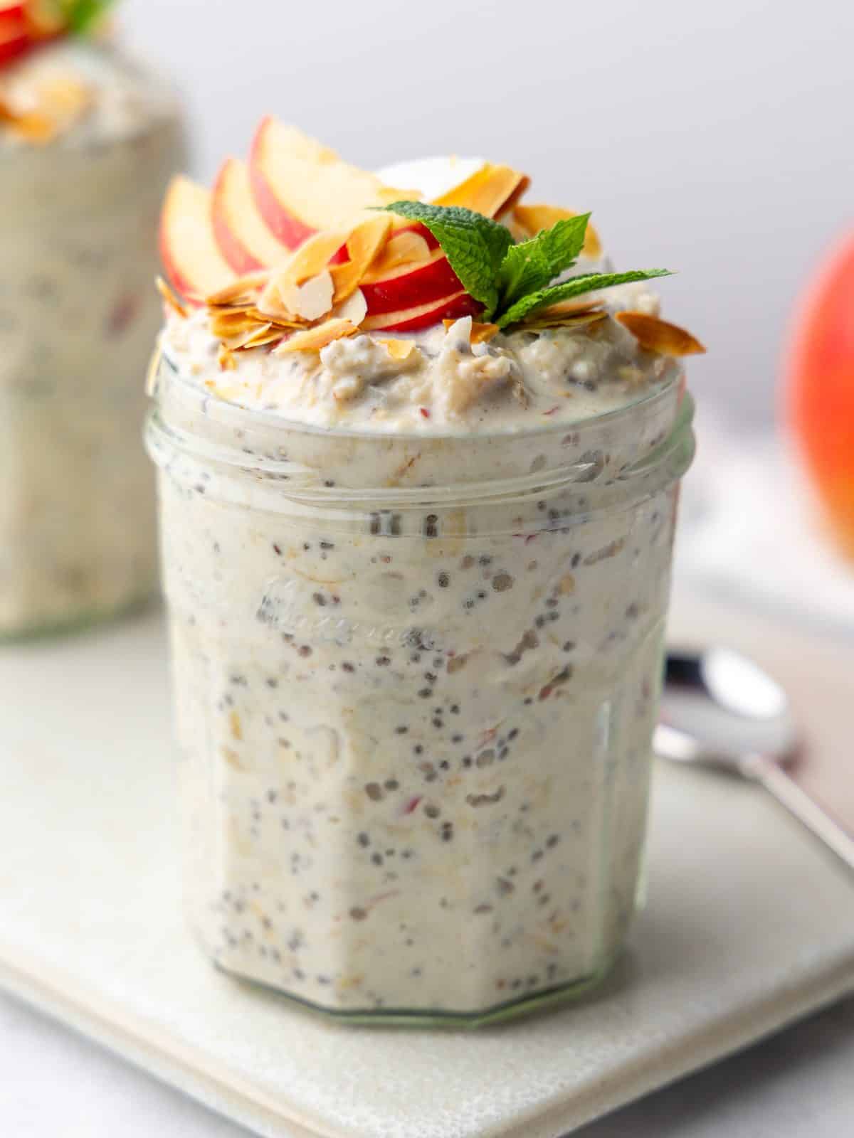 Close up of creamy bircher muesli with chia seeds and grated apple in a glass jar with toasted almonds on top