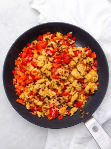 Crumbled turkey breakfast sausage and diced red bell pepper browning in a skillet