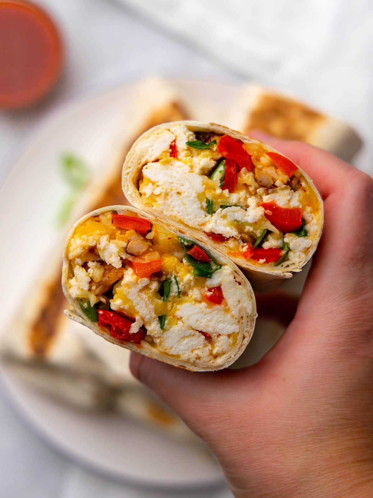 Hand holding a high protein low calorie breakfast burrito cut in half to show the filling